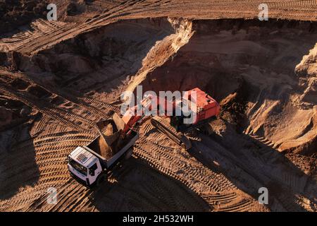 Der Bagger lädt den Sand in einen Muldenkipper im Tagebau. Entwicklung des Sandes im Tagebaus. Schwere Maschinen auf Erdarbeiten im Steinbruch. Miningtruck Stockfoto