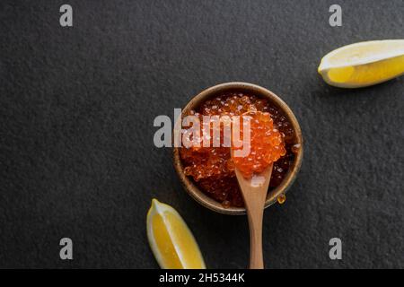 Frischer roter Kaviar mit einem Holzlöffel auf dunklem Grund, in einer Keramikschale. Copyspace Stockfoto