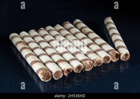 Süße Stäbchen mit Füllung auf dem Tisch mit Reflexion. Dessert für Tee auf schwarzem Hintergrund Stockfoto