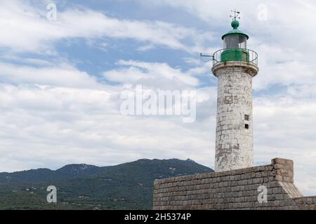 Alter weißer Leuchtturmturm mit grüner Oberseite, montiert auf Steinpier. Eingang zum Hafen von Propriano, Insel Korsika, Frankreich Stockfoto