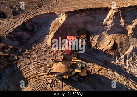 Der Bagger lädt den Sand in einen Muldenkipper im Tagebau. Entwicklung des Sandes im Tagebaus. Schwere Maschinen auf Erdarbeiten im Steinbruch. Miningtruck Stockfoto