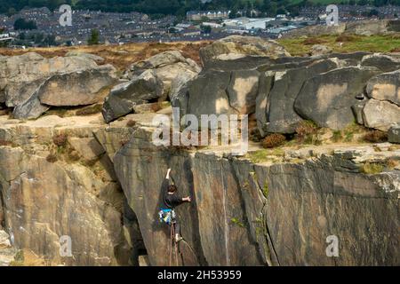 Kletterer mit traditioneller Ausrüstung an der Spitze eines Felskletterns im Ilkley Quarry an den Cow und Calf Rocks mit Blick auf die Stadt Ilkley. Yorkshire, Großbritannien Stockfoto