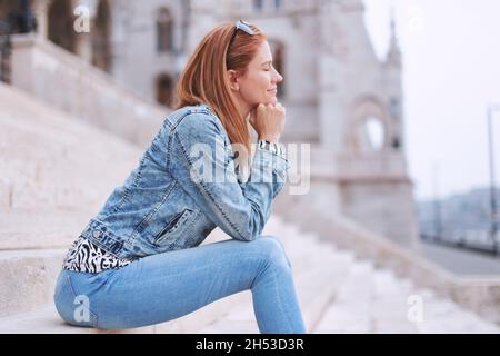 Junge kaukasische Rothaarige Frau, die sich auf Treppen in der Stadt im Freien ausruht Stockfoto