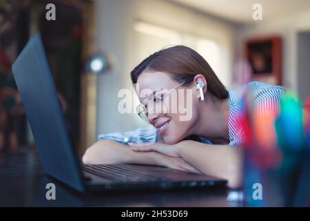Glückliche junge positive kaukasische Frau mit Freisprecheinrichtung lächelt am Laptop Stockfoto