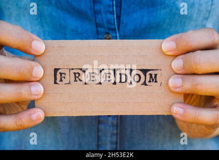 Frau Hände halten Pappkarte mit Wort Freiheit von schwarzen Alphabet Marken gemacht. Stockfoto