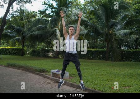 Sportlich aktiver junger Mann in Sportbekleidung, der im Park Sportübungen macht. Glücklich fit Mann springen im Freien. Gesundes Lifestyle-Konzept, Sport im Freien Stockfoto