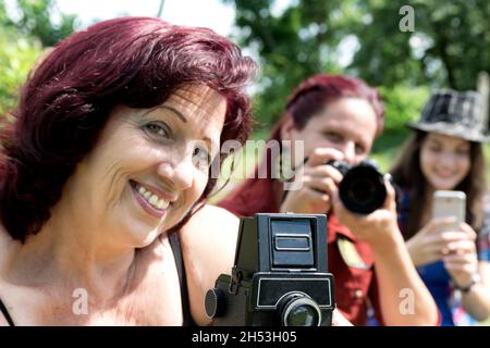 Selektiver Fokus des vorderen Teils einer alten Kamera in der unteren Bildmitte befinden sich drei Frauengesichter verschiedener Generationen dahinter Stockfoto