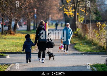 Riga, Lettland, 2. November 2021: Eine Frau mit einem Kind und einem Hund auf einem Bürgersteig in einer Herbststadt, Rückansicht Stockfoto