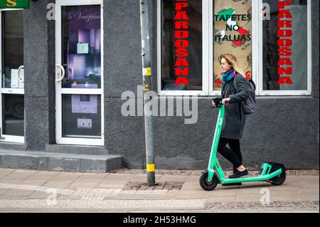 Riga, Lettland, 2. November 2021: Eine junge Frau mit einem Elektroroller an einer Fußgängerüberführung Stockfoto