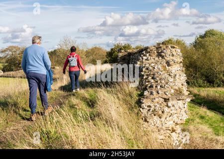 Ein paar Touristen - ein verheirateter Mann und eine verheiratete Frau - gehen neben einem Abschnitt der ruinierten römischen Stadtmauer in Silchester. Hampshire, Großbritannien Stockfoto