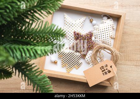 Geschenkbox mit Weihnachtsspielzeug aus Stoff auf Holzhintergrund, im Vordergrund ein Tannenzweig im Unschärfe-Effekt. Ökologisches Verpackungskonzept, Null Stockfoto