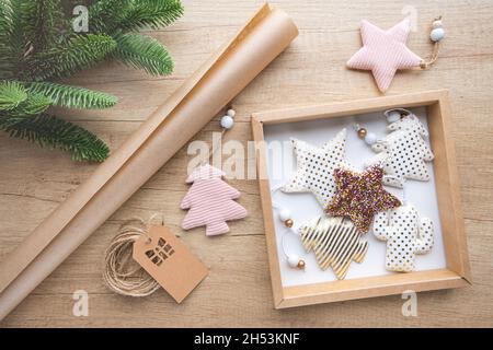 Geschenkbox mit Weihnachtsspielzeug aus Stoff, Rolle Kraftpapier, Tannenzweig auf Holzhintergrund. Eco-Verpackungskonzept, keine Verschwendung. Geschenkverpackung Stockfoto