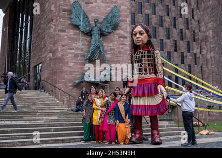 Die kleine Amal freut sich über viele Zuschauer, die durch das Stadtzentrum spazieren, wo sie am 27. Oktober 2020 in Coventry, Großbritannien, mit asiatischen Tänzern in hellen Saris vor der Coventry Cathedral tanzen sieht. Little Amal ist eine 3.5 Meter große Marionette und ein lebendiges Kunstwerk eines jungen syrischen Flüchtlingskindes, das in den letzten 3 Monaten 8000 km von der Grenze zu Syrien durch die Türkei, Griechenland, Italien, Frankreich, die Schweiz, Deutschland, Belgien und das Vereinigte Königreich konzentrieren ihre Aufmerksamkeit auf die dringenden Bedürfnisse junger Flüchtlinge. Coventry, das das größte syrische Neuansiedlungsprogramm in der Region hat, und auch a la Stockfoto