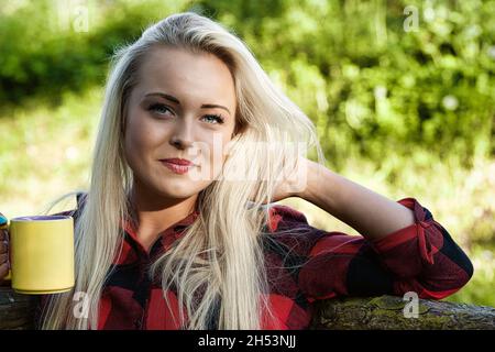 Porträt einer jungen Frau mit langen blonden Haaren im Freien, im Wald oder in einem Park, mit einem schönen heißen Tee Stockfoto