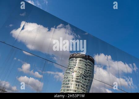 Die Fassade des Grand Central Station aus Metall spiegelt den blauen Himmel, die Wolken und das ikonische Rotunda-Gebäude am 15. Oktober 2021 in Birmingham, Großbritannien, wider. Grand Central ist ein Einkaufszentrum in Birmingham, England, das am 24. September 2015 eröffnet wurde. Es gehört derzeit Hammerson und CPPIB. Das ursprüngliche Zentrum wurde 1971 als Teil des Wiederaufbaus des Bahnhofs Birmingham New Street erbaut. Es war bekannt als Birmingham Shopping Centre, bevor es in Pallasades umbenannt wurde. Im Rahmen der Neuentwicklung des New Street Station Gateway Plus wurde Grand Central einem großen Überschuß unterzogen Stockfoto