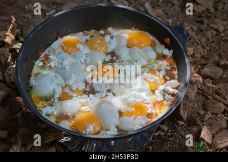 Shakshouka, ein traditionelles Gericht aus pochierten Eiern in Sauce aus Tomaten, Harissa, Olivenöl, Zwiebeln, Knoblauch und Gewürzen, In einer Pfanne im Freien gekocht Stockfoto