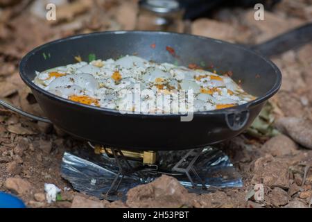 Shakshouka, ein traditionelles Gericht aus pochierten Eiern in Sauce aus Tomaten, Harissa, Olivenöl, Zwiebeln, Knoblauch und Gewürzen, In einer Pfanne im Freien gekocht Stockfoto