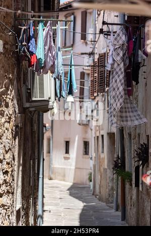 Koper, Slowenien - 12. Juli 2021: Enge Straße zwischen alten, baufälligen Stadthäusern. Kleidung hing zwischen Gebäuden. Stockfoto