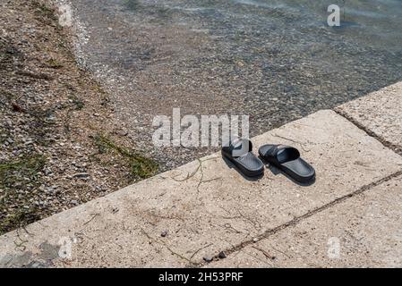 KOPER, SLOWENIEN - 12. JULI 2021: Badeschlappen auf einem Betonblock an einem Kiesstrand über der Adria. Stockfoto