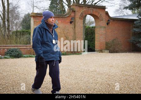 Ältere asiatische indische Frau, die im Winter im Freien geht, Sport macht, Großbritannien. Tragen Sie warme Kleidung und einen SOS-Anhänger mit persönlichem Sicherheitsalarm Stockfoto