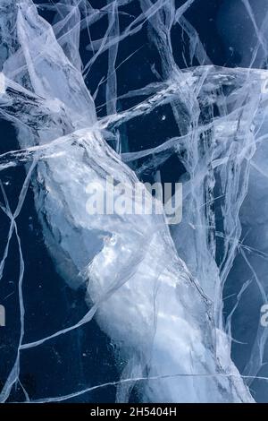 Ein großer Riss im Eis mit kleinen Rissen um das Eis herum. Blaues transparentes Eis. Vertikal. Stockfoto