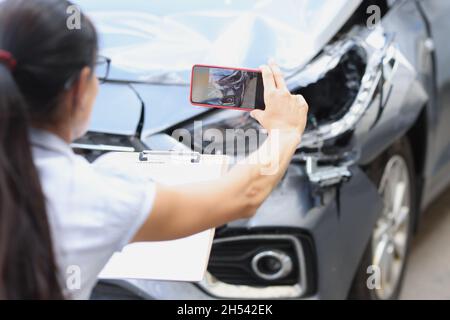 Versicherungsagentin, die Fotos von einem defekten Auto aus der Nähe des Mobiltelefons gemacht hat Stockfoto