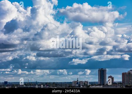 Silhouette eines Flugzeugs, das vor dem Hintergrund von Kumuluswolken über die Stadt fliegt Stockfoto