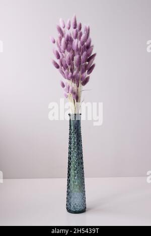 Glasvase mit lila getrockneten Blumen auf Tischhintergrund stehen Stockfoto