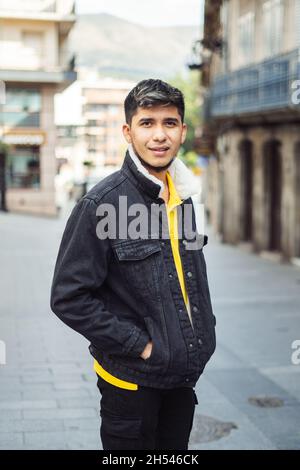 Junger Spanier mit Händen in der Jackentasche, der direkt auf die Kamera schaut und lächelt. Stockfoto