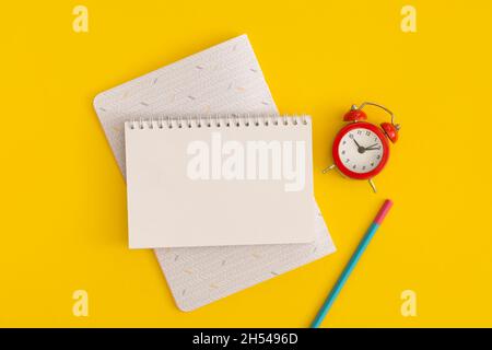 Roter Wecker und Notizbücher mit Platz für Text auf gelbem Hintergrund Stockfoto