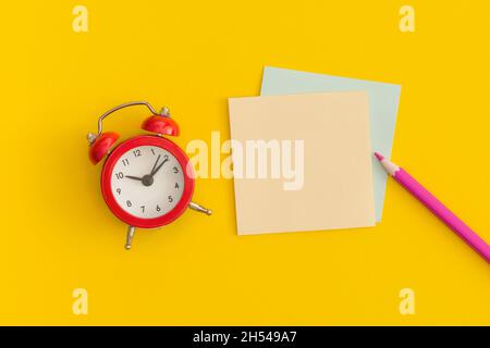 Roter Wecker und Haftnotizen mit Platz für Text auf gelbem Hintergrund Stockfoto
