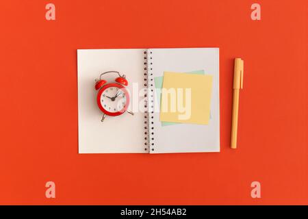 Roter Wecker und Notizbücher mit Platz für Text auf rotem Hintergrund Stockfoto