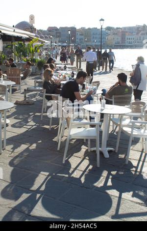 Chania, Kreta - Griechenland - Oktober 20 2021 : sonnenbeschienes Straßencafé am historischen venezianischen Hafen Urlauber entspannen sich bei einem Drink am späten Nachmittag Stockfoto