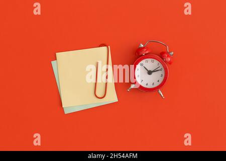 Roter Wecker und Haftnotizen mit Platz für Text auf rotem Hintergrund Stockfoto