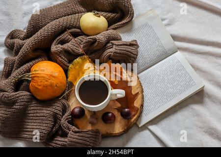 Herbst dekoriert Hintergrund mit Kaffeetasse und Buch im Bett. Nahaufnahme, selektiver Fokus Stockfoto