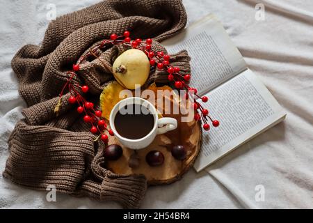 Tasse Kaffee und offenes Buch auf dem herbstlich dekorierten Schreibtisch mit Pullover und Kürbis. Nahaufnahme, selektiver Fokus Stockfoto