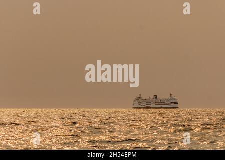 Eine Passagierfähre überquert an einem Sommermorgen die Straße von Georgia, mit dichtem Rauch von Waldbränden, die die Sonne verdunkeln und Meer und Himmel orange werden lassen. Stockfoto