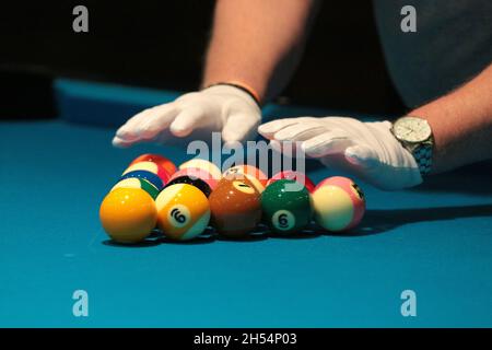 Ein Schiedsrichter überprüft mit weißen Handschuhen die Billardkugeln, die in einem Dreieck liegen. Stockfoto