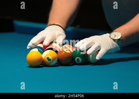 Ein Schiedsrichter überprüft mit weißen Handschuhen die Billardkugeln, die in einem Dreieck liegen. Stockfoto