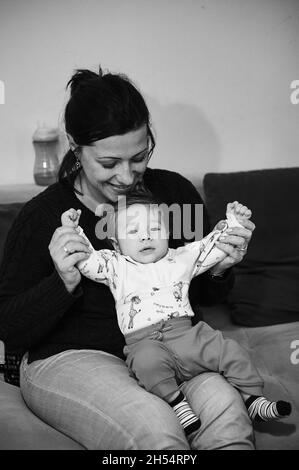 Graustufen der kaukasischen Mutter, die mit ihrem Kleinkind auf dem Schoß spielt Stockfoto