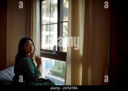 asiatische Frau sitzt neben dem Fenster mit Smartphone-Videoanruf einschalten Stockfoto