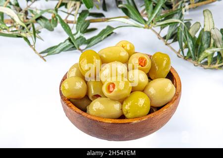 Eingelegte kleine grüne Oliven, gefüllt mit rotem Paprika in einer Holzschüssel. Früchte von Olea europaea, gefüllt mit Paprika-Scheiben. Nahaufnahme von Abov Stockfoto