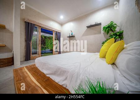 Holzschrank mit Uhr neben dem Stuhl am Schreibtisch im gemütlichen Schlafzimmer mit Bett an der Wand Stockfoto