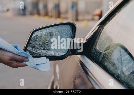 Männliche Hand Reinigung Auto im Freien mit Lappen, wischen Wasser mit Mikrofaser Tuch auf der Seite Rückspiegel Stockfoto