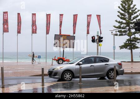 Manly Beach Sydney, Surfer geht an einem elektronischen Schild vorbei, das die Gemeinschaft ermutigt, sicher zu sein, Sydney, Australien Stockfoto