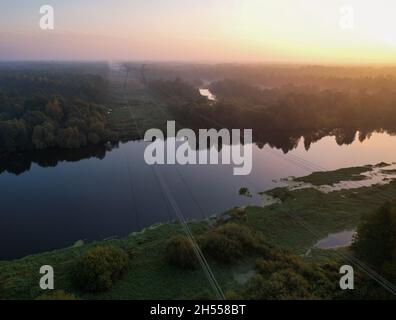 Hochspannungskabel, die in einem bewaldeten Gebiet über einen Fluss geschleudert werden. Stockfoto