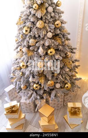 Weihnachtsgeschenke unter Neujahrsbaum mit Kunstschnee mit goldener Beleuchtung. Goldene Farbe. Stockfoto