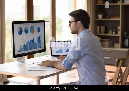 Fokussierte intelligente junge Geschäftsmann mit Gadgets Analyse von Statistiken. Stockfoto