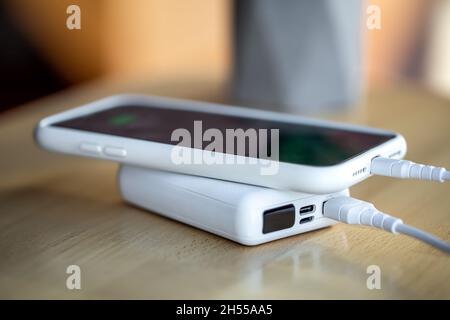 Ein Smartphone wird von einer kleinen weißen Powerbank geladen. Stockfoto