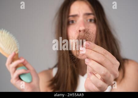 Haarausfall bei Frauen. Junge Frau ist wegen Haarausfall aufgeregt. Portrait von frustrierten Mädchen mit Problemhaar, isoliert. Besorgt Mädchen hält lange Stockfoto